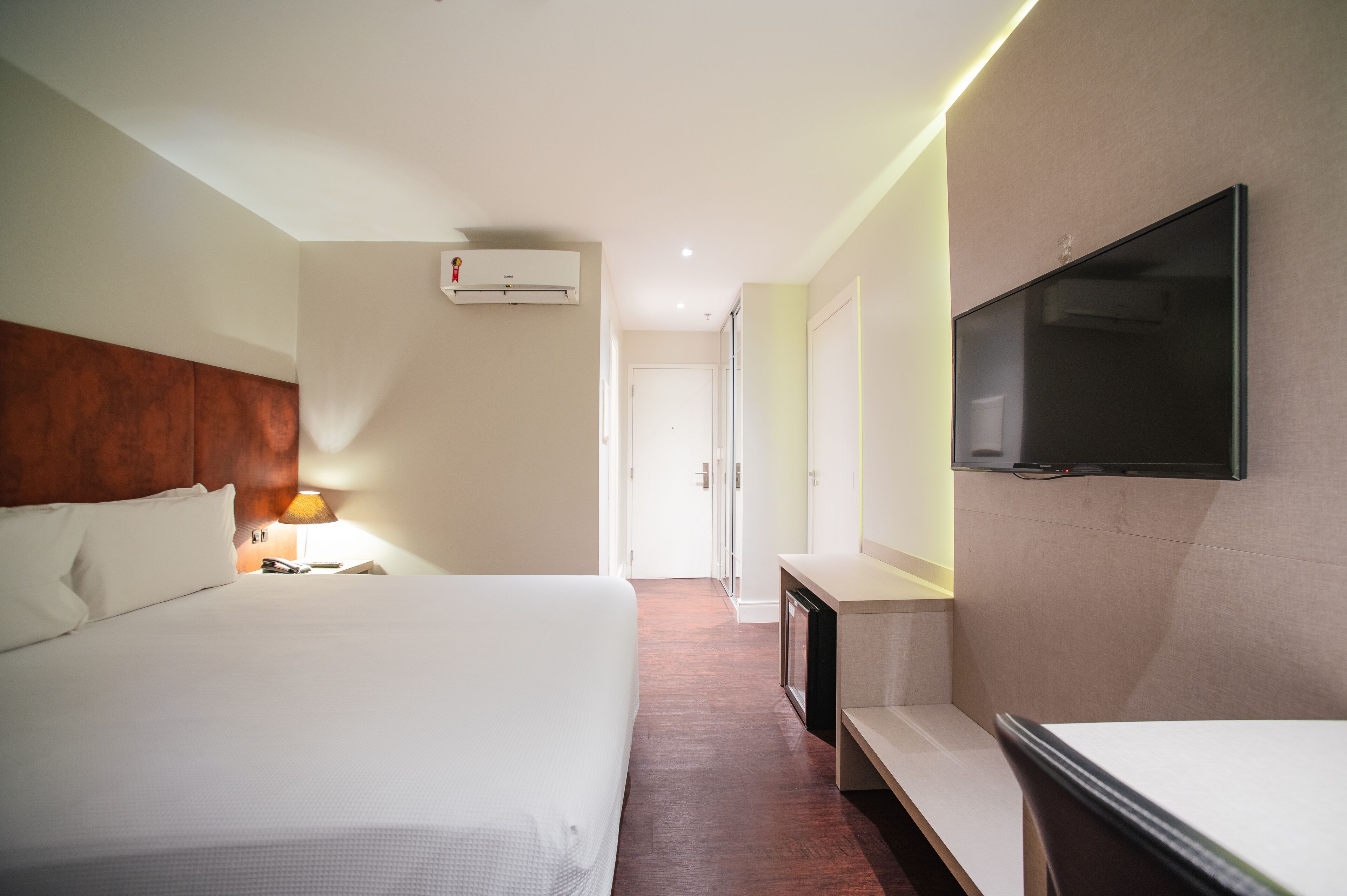 Una habitación de hotel con una cama grande, televisión montada en la pared, un escritorio y una lámpara.