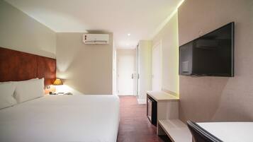 Una habitación de hotel con una cama grande, televisión montada en la pared, un escritorio y una lámpara.