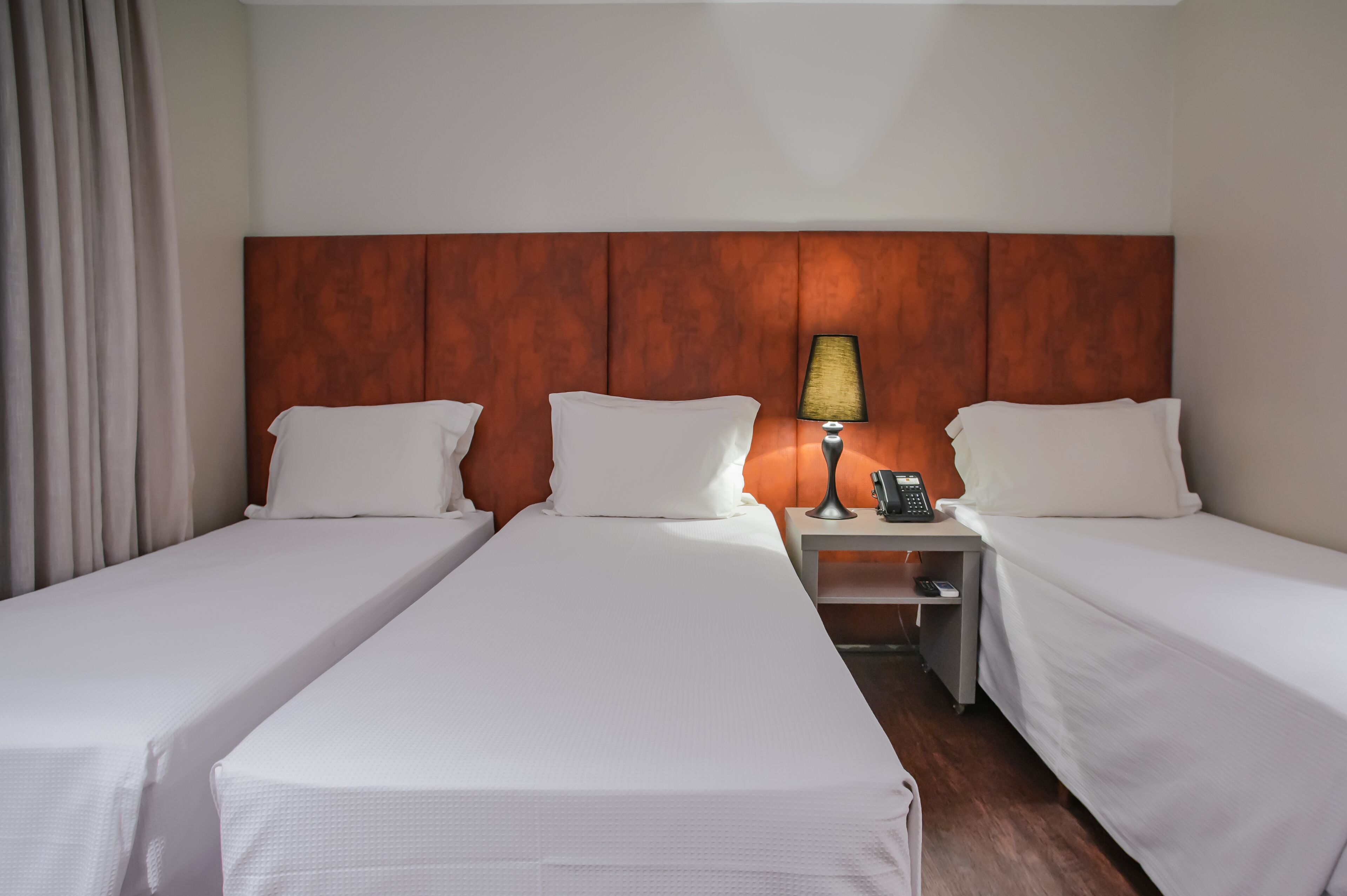 A hotel room with two single beds, a wooden headboard, a bedside table with a lamp, and a phone.