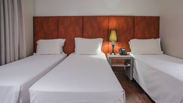 Quarto de hotel com duas camas de solteiro, cabeceira de madeira, mesa de cabeceira com abajur e telefone.
