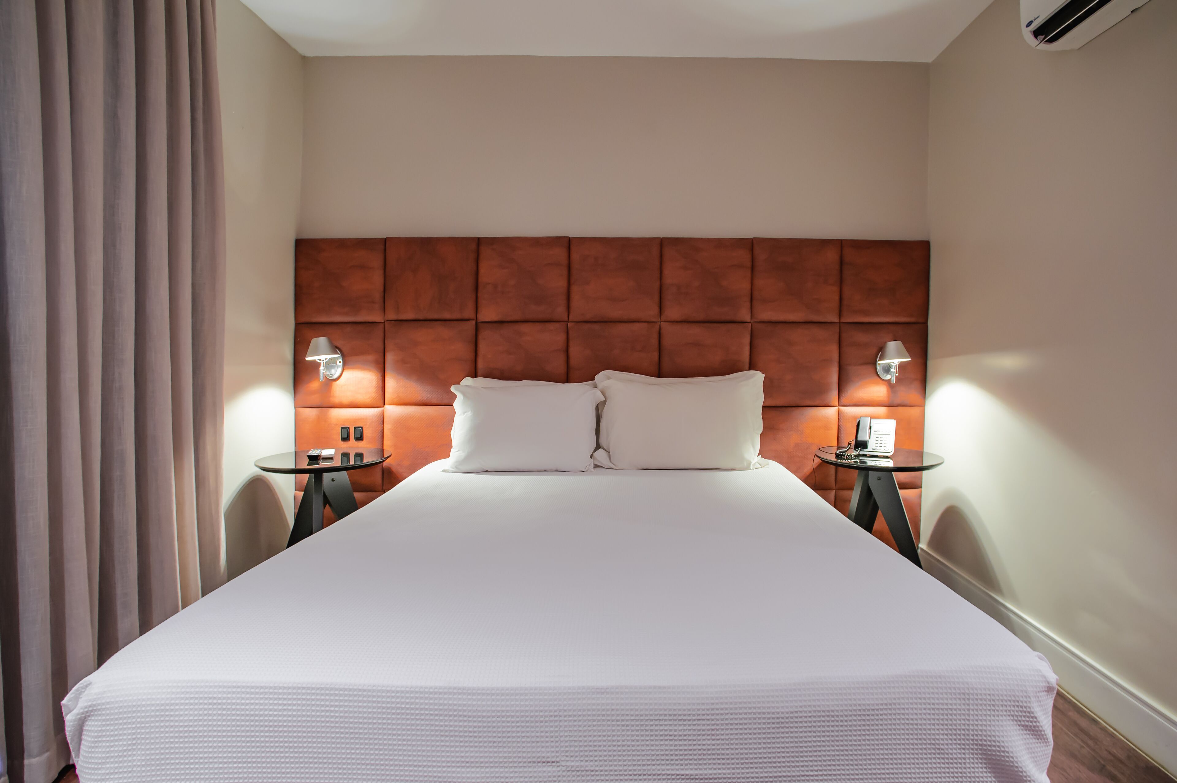 A hotel room with a large bed, two bedside tables, a wooden headboard, and a telephone on one of the tables.