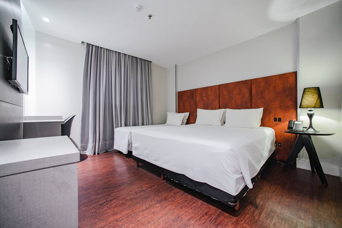 A hotel room with a large bed, a desk, a TV, and a lamp.