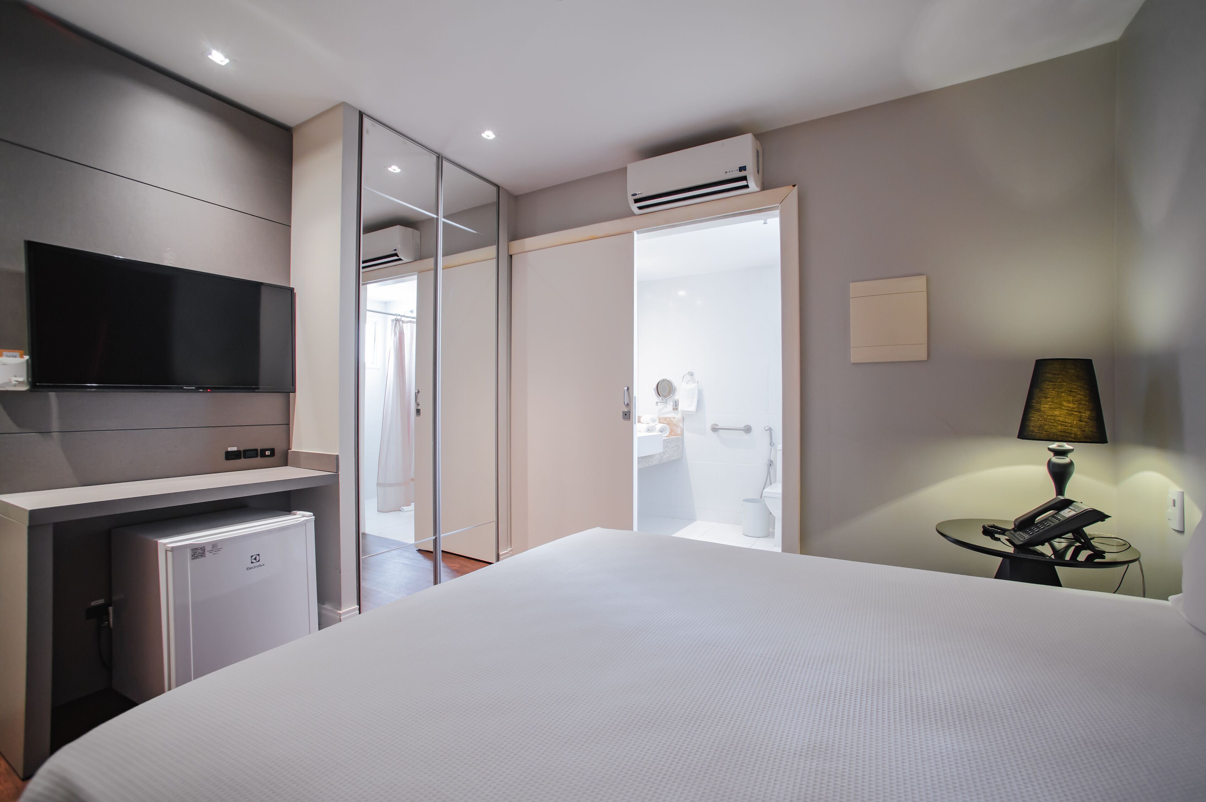 Une chambre d’hôtel équipée d’un lit, d’une télévision, d’un mini-réfrigérateur, d’un bureau avec une lampe et d’un miroir.