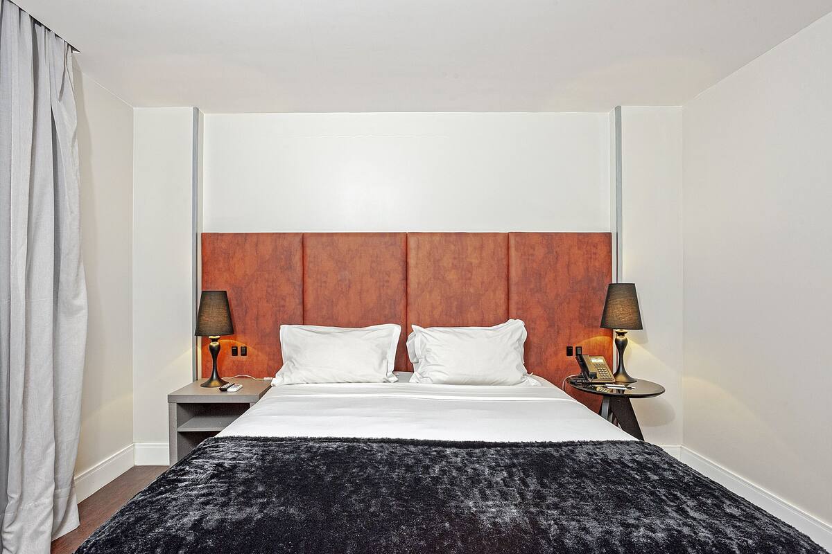A hotel room with a bed, two bedside tables, a lamp, and a telephone.