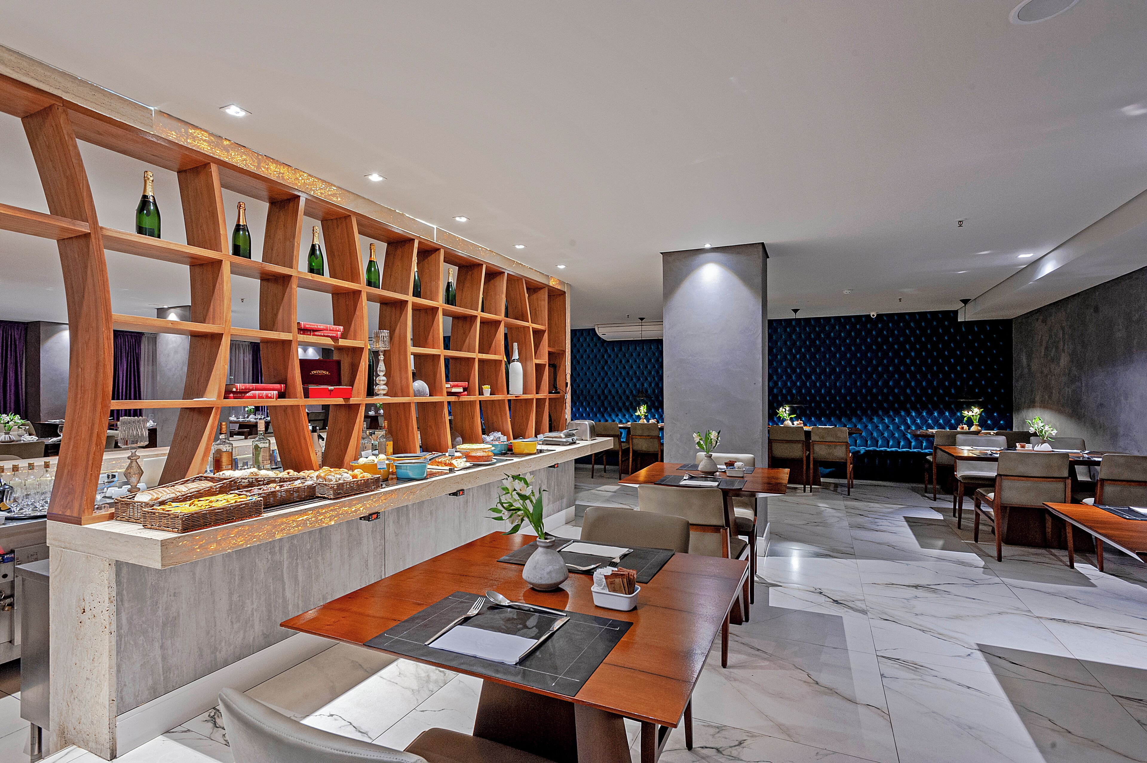 A modern restaurant with wooden shelves, marble flooring, and a blue acoustic panel wall.