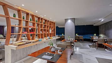 A modern restaurant with wooden shelves, marble flooring, and a blue acoustic panel wall.