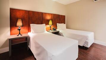 A hotel room with two single beds, a nightstand with a lamp, a phone, and an air conditioning unit on the wall.