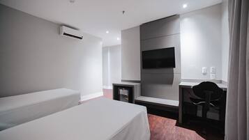 Habitación de hotel con cama, escritorio, silla, televisor y aire acondicionado.