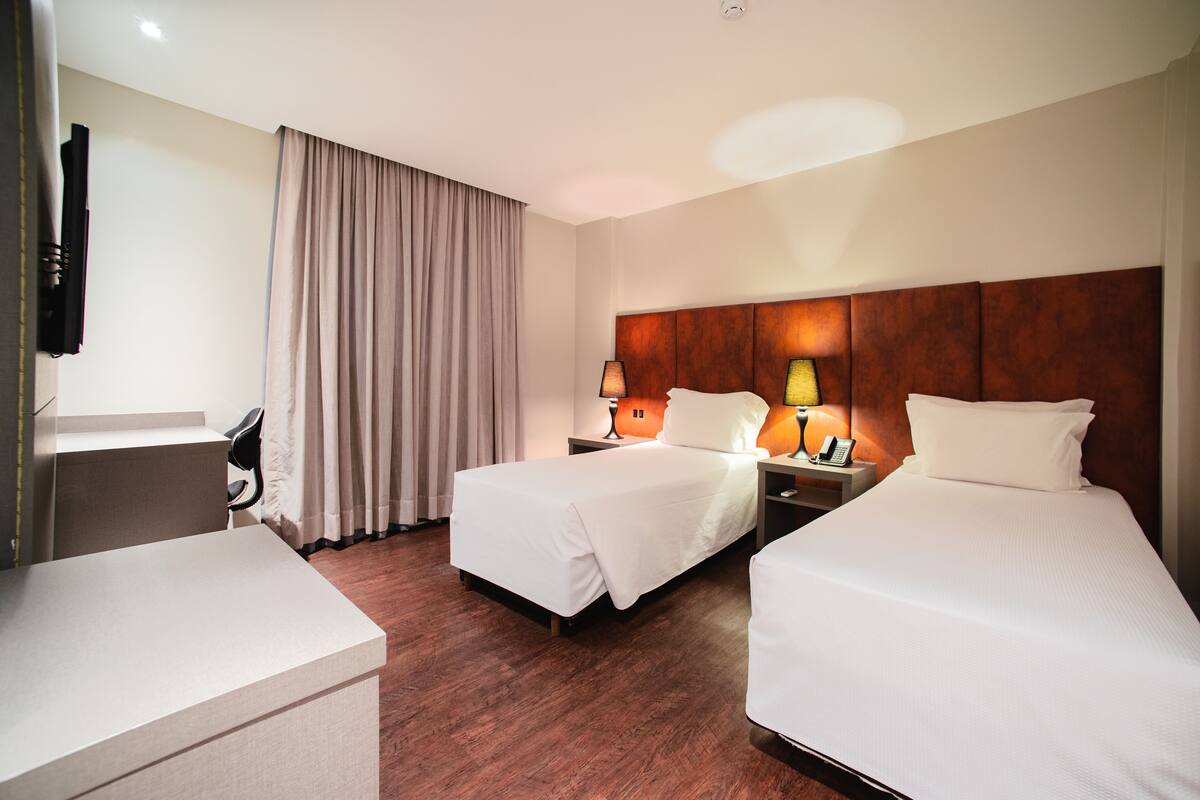 A hotel room with two beds, a desk, a chair, a TV, and a curtain.