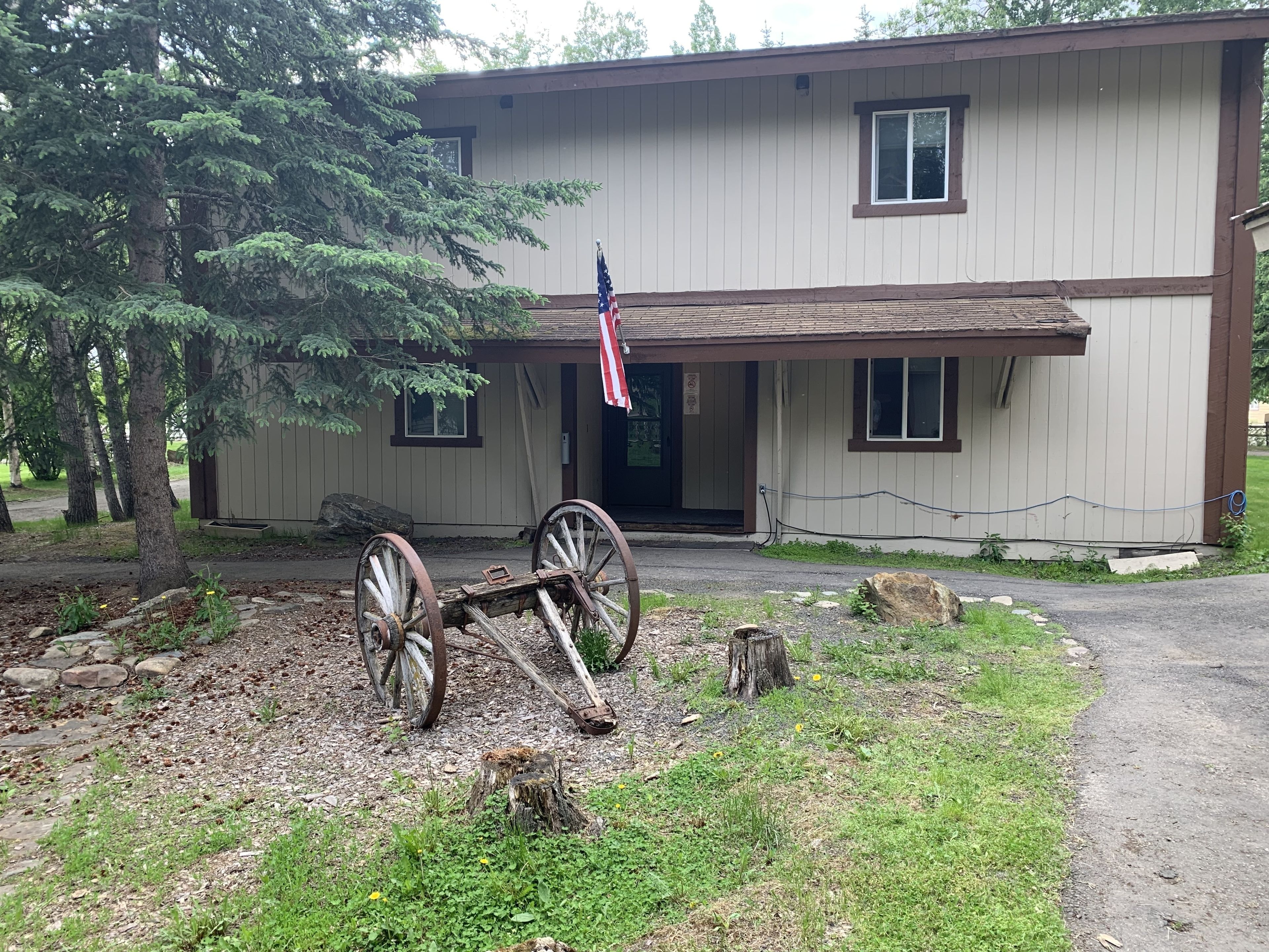 A two-story building with a front porch, an American flag, and a vintage wooden cart.