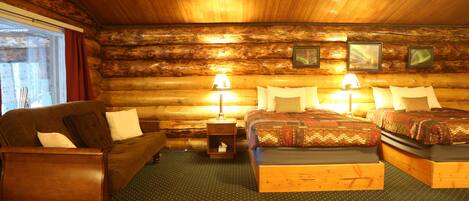 A log cabin-style bedroom with two beds, a sofa, and a nightstand with lamps.