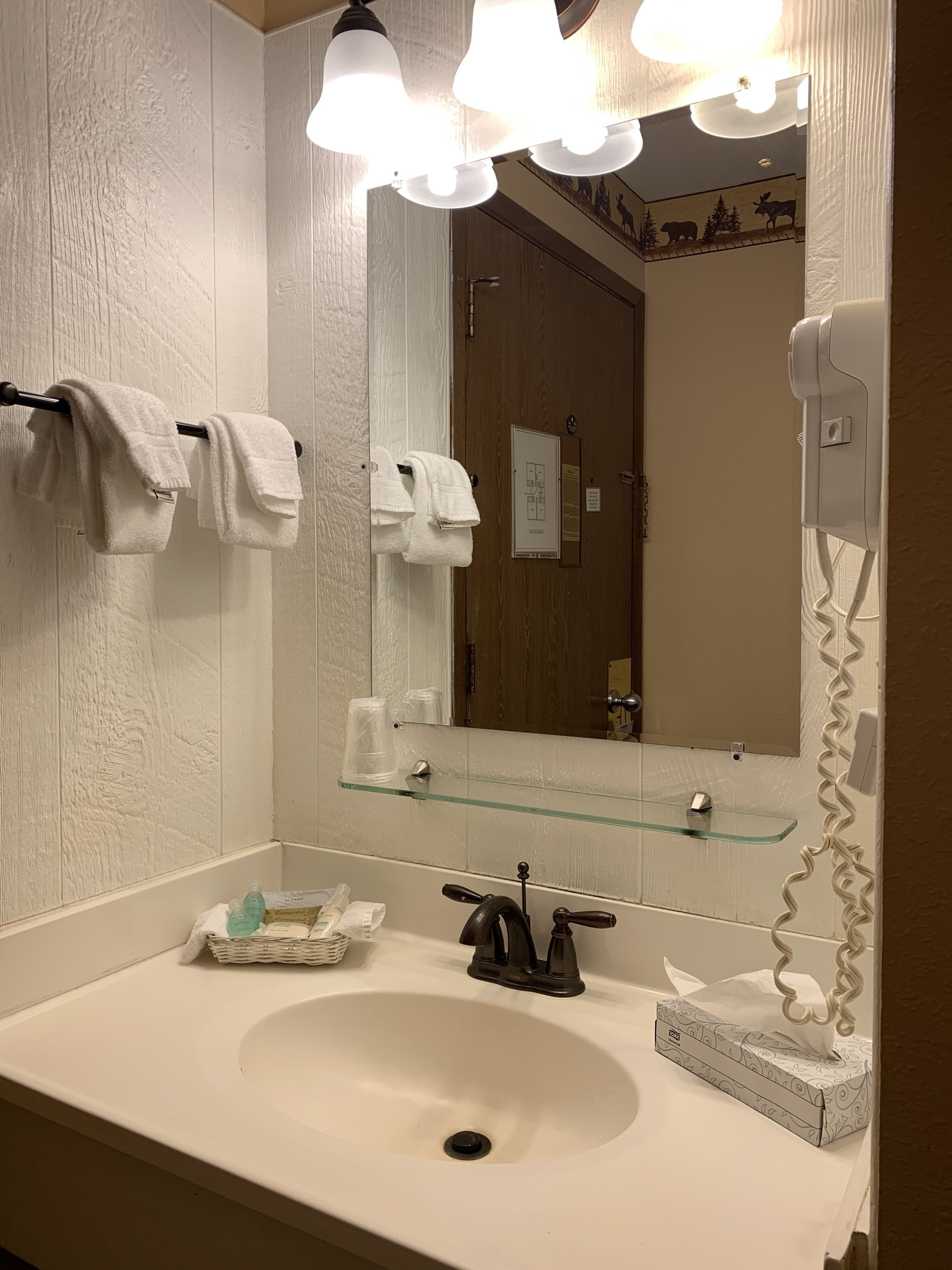 A bathroom with a white sink, a glass shelf, a towel rack with white towels, a mirror, and a hairdryer.