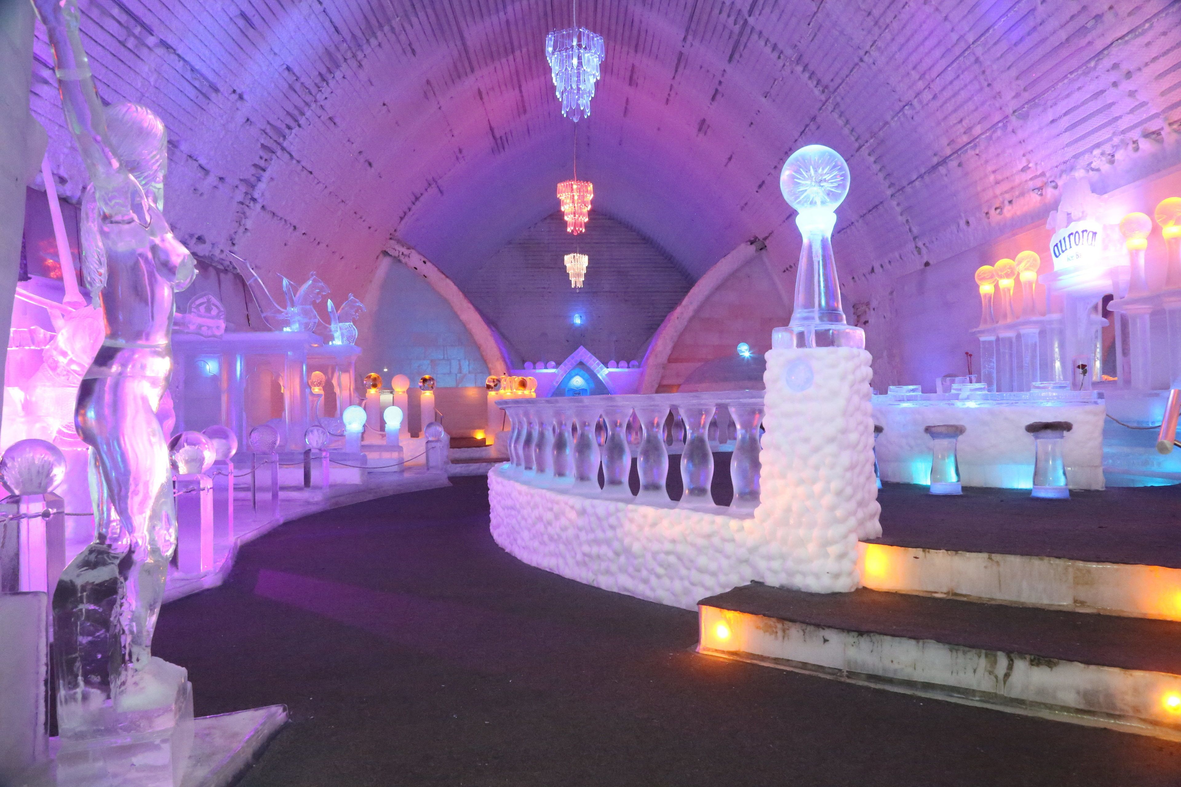 An ice sculpture exhibit with illuminated sculptures and chandeliers in a dome-shaped room.