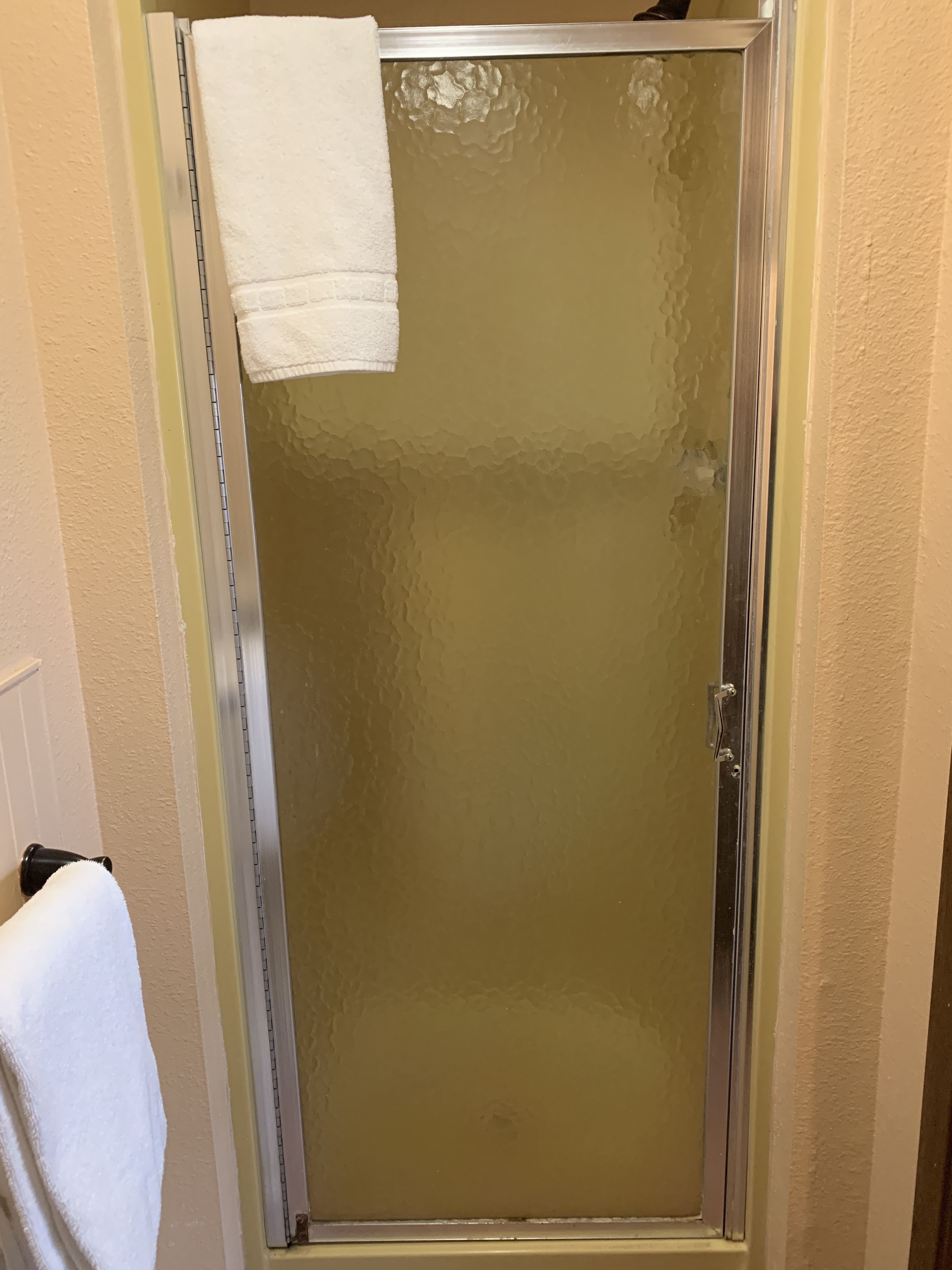 A bathroom with a glass shower door, a white towel hanging on the wall, and a visible towel rack.