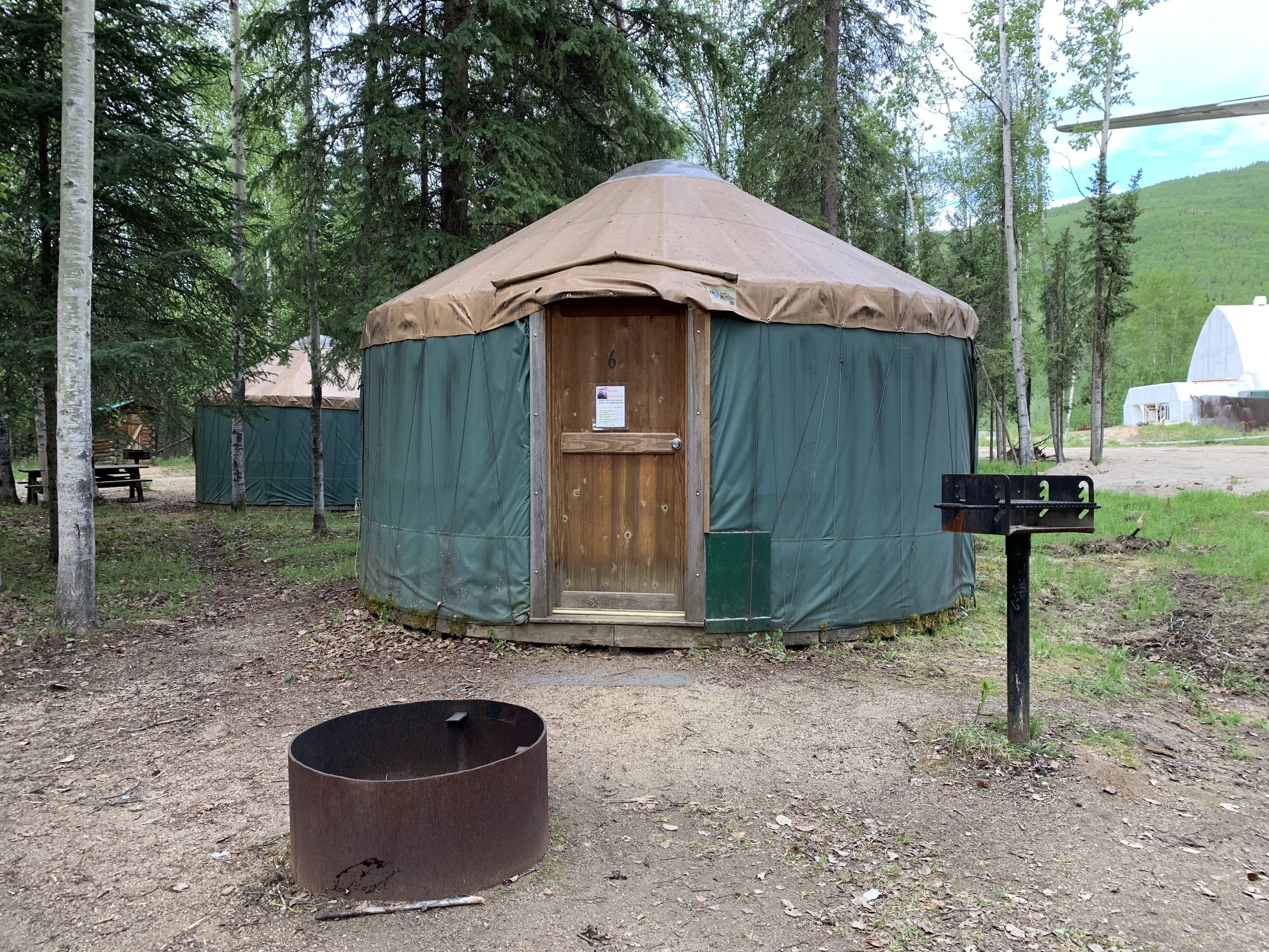 A yurt with a wooden door, a metal fire pit, and a signpost in a forested area.