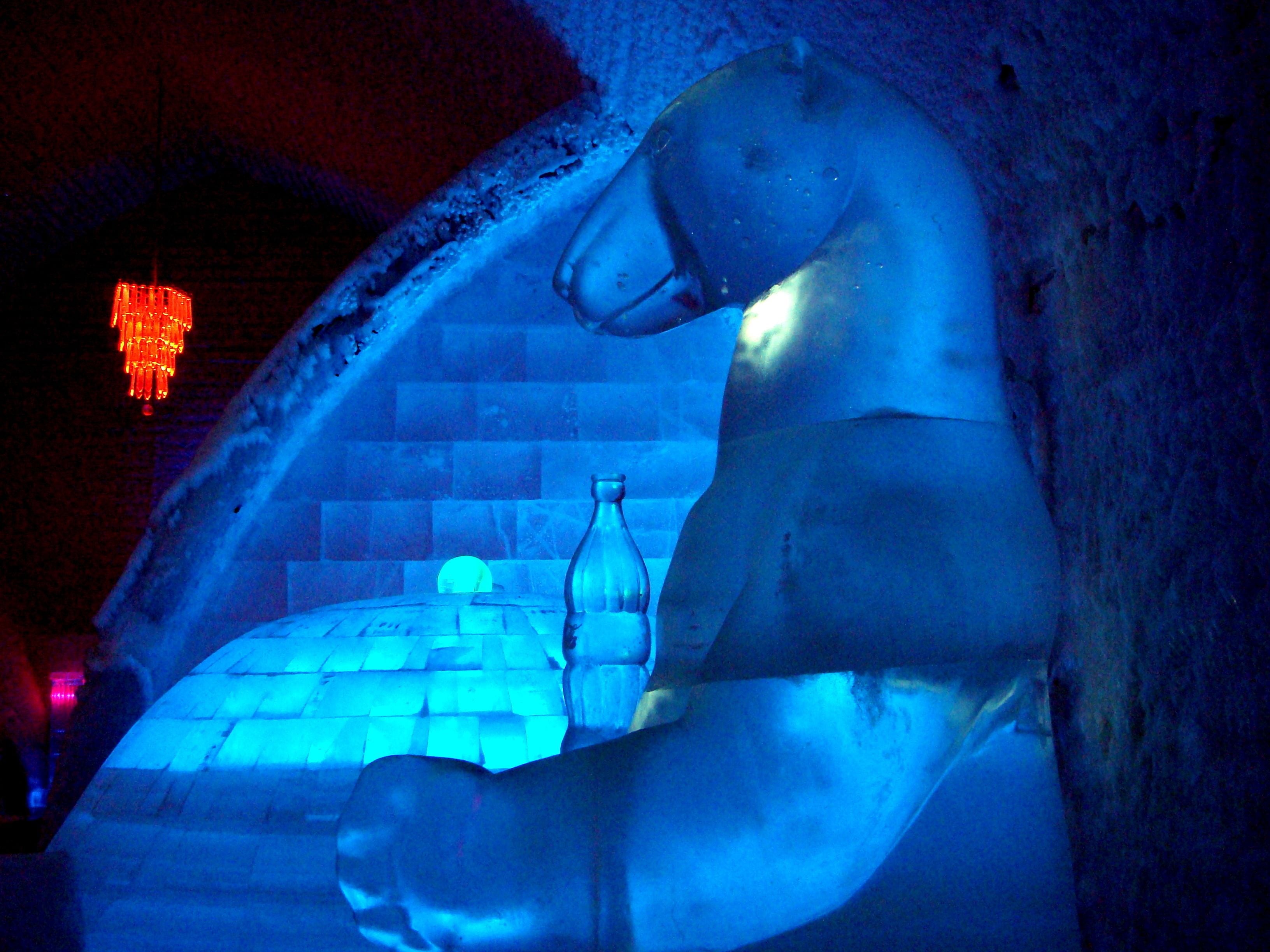 Un'imponente scultura di ghiaccio a forma di orso in una stanza scarsamente illuminata, con parete in mattoni e lampadario rosso.