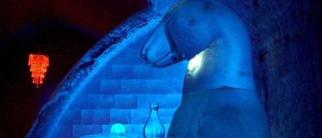 Un'imponente scultura di ghiaccio a forma di orso in una stanza scarsamente illuminata, con parete in mattoni e lampadario rosso.