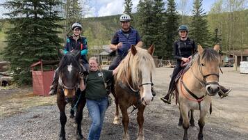 Three people on horseback in an outdoor setting with trees and a gravel path.