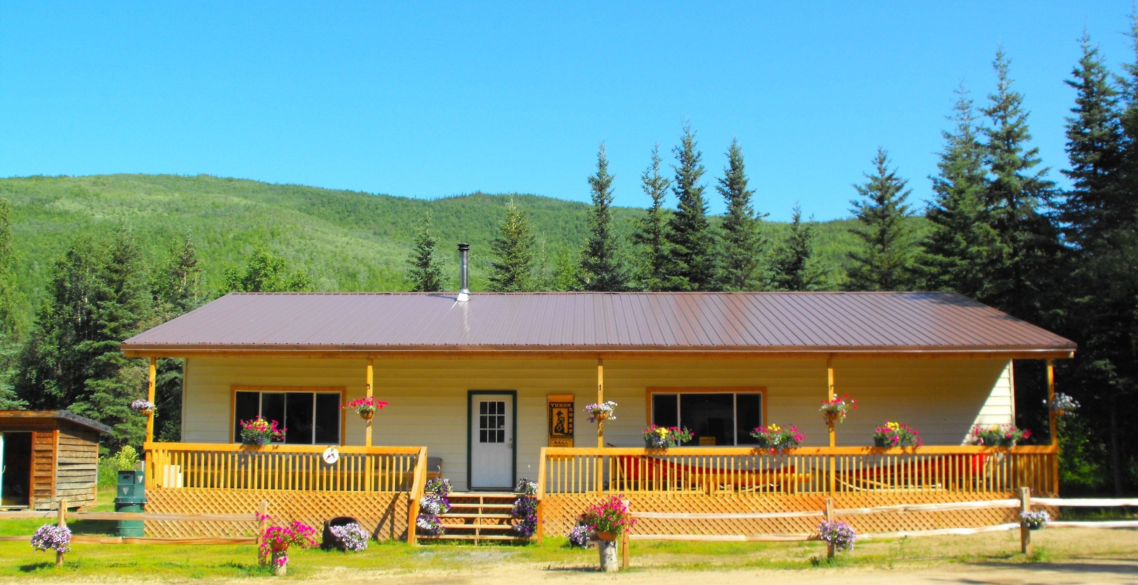 A two-story lodge with a wooden deck, a front porch with steps, and a mountain backdrop.