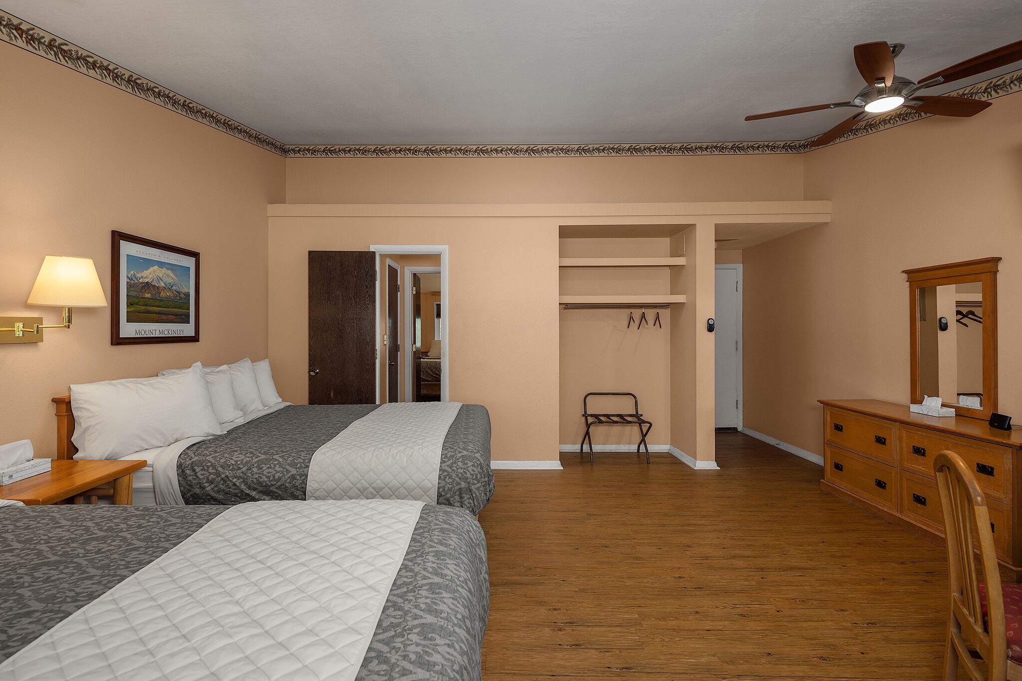 A hotel room with two beds, a dresser, a mirror, a ceiling fan, and a door leading to a closet.