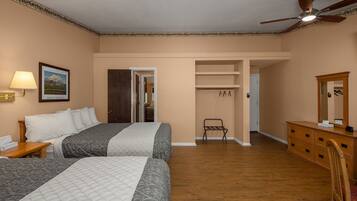 A hotel room with two beds, a dresser, a mirror, a ceiling fan, and a door leading to a closet.