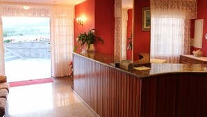 A hotel reception area with a red wall, a large mirror, and a plant on the counter. - Hotel Xacobeo (Sanxenxo)