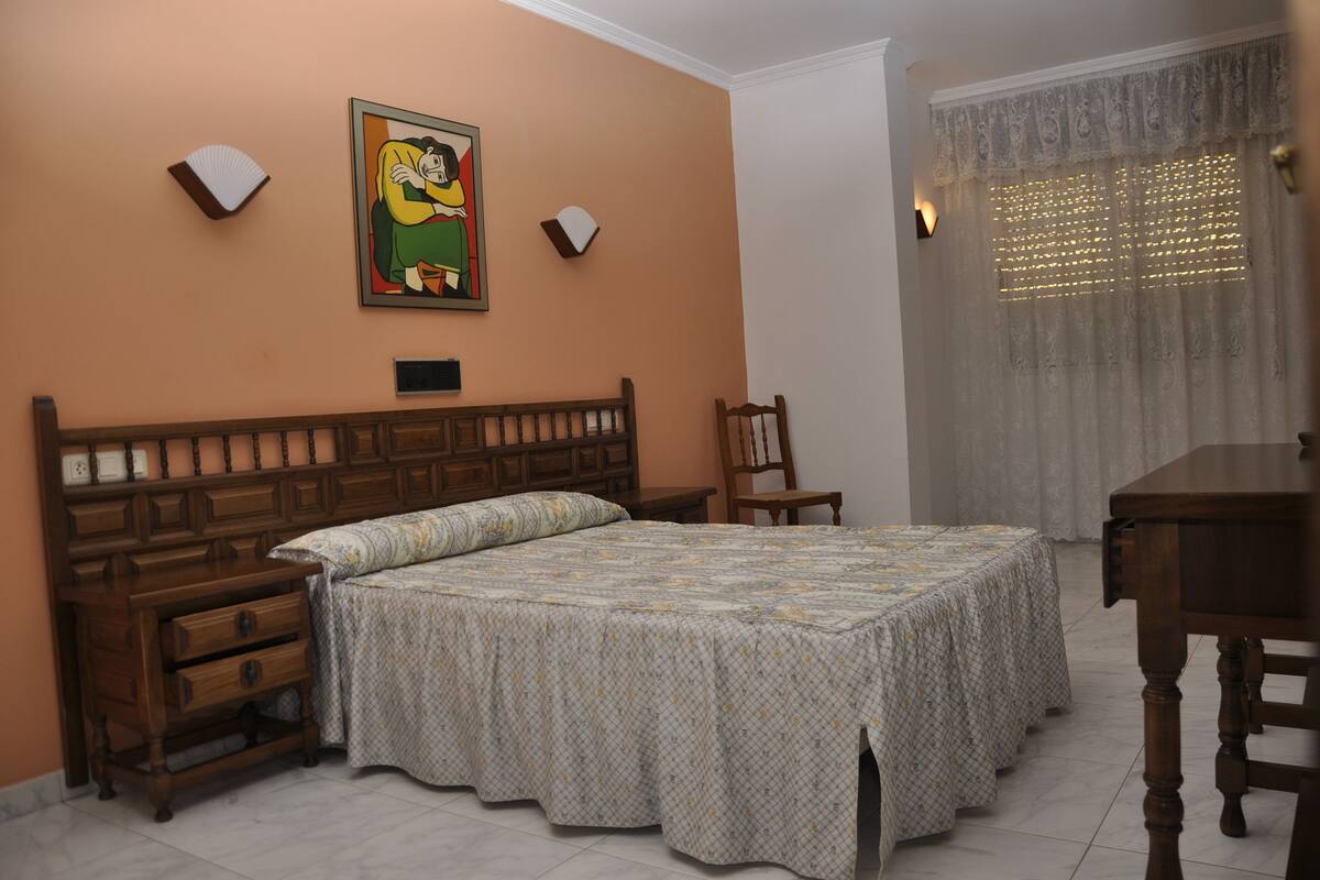 A bedroom with a wooden bed, a nightstand, a chair, and a table.