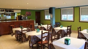 A restaurant with multiple tables and chairs, a bar area, and a green wall with windows. - Hotel Xacobeo (Sanxenxo)