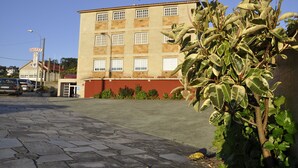 A hotel with a red and beige facade, multiple windows, and a paved parking area. - Hotel Xacobeo (Sanxenxo)