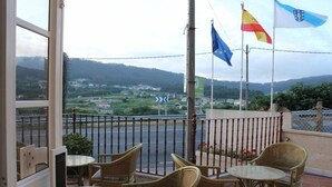 A balcony with wicker furniture and flags, overlooking a road and greenery. - Hotel Xacobeo (Sanxenxo)