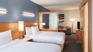 A hotel room with two beds, a wooden headboard, bedside lamps, a desk with a lamp, a television, a sofa, and a large mirror. - SpringHill Suites by Marriott Houston Northwest (Houston)