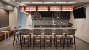 A modern bar area with a long counter, multiple bar stools, and a television mounted on the wall. - SpringHill Suites by Marriott Houston Northwest (Houston)
