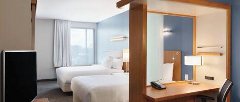 Habitación de hotel con dos camas, un escritorio con silla, televisión y un espejo grande.