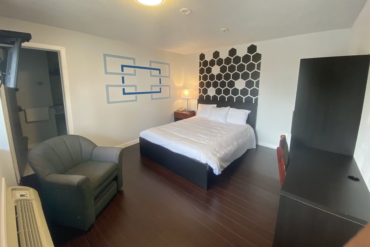 A hotel room with a bed, a chair, a desk, and a TV.