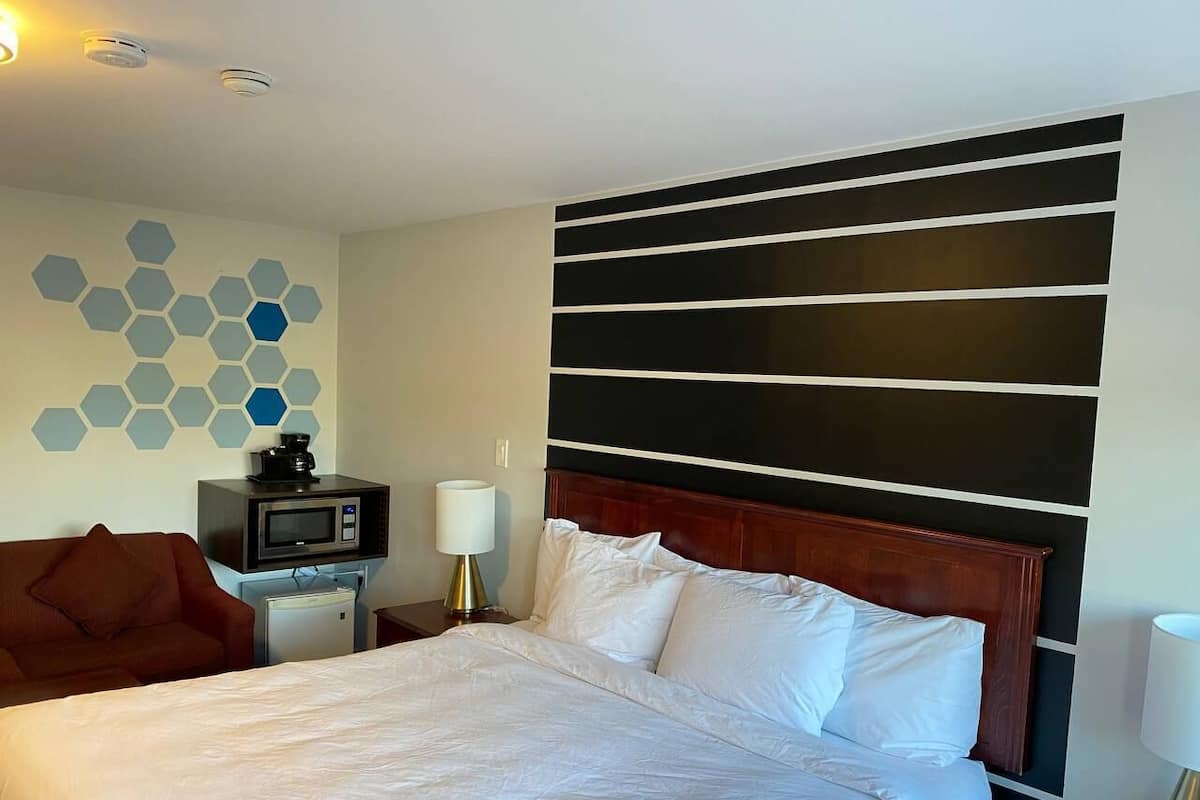 A hotel room with a large bed, a wooden headboard, a TV, and a wall with hexagonal patterns.