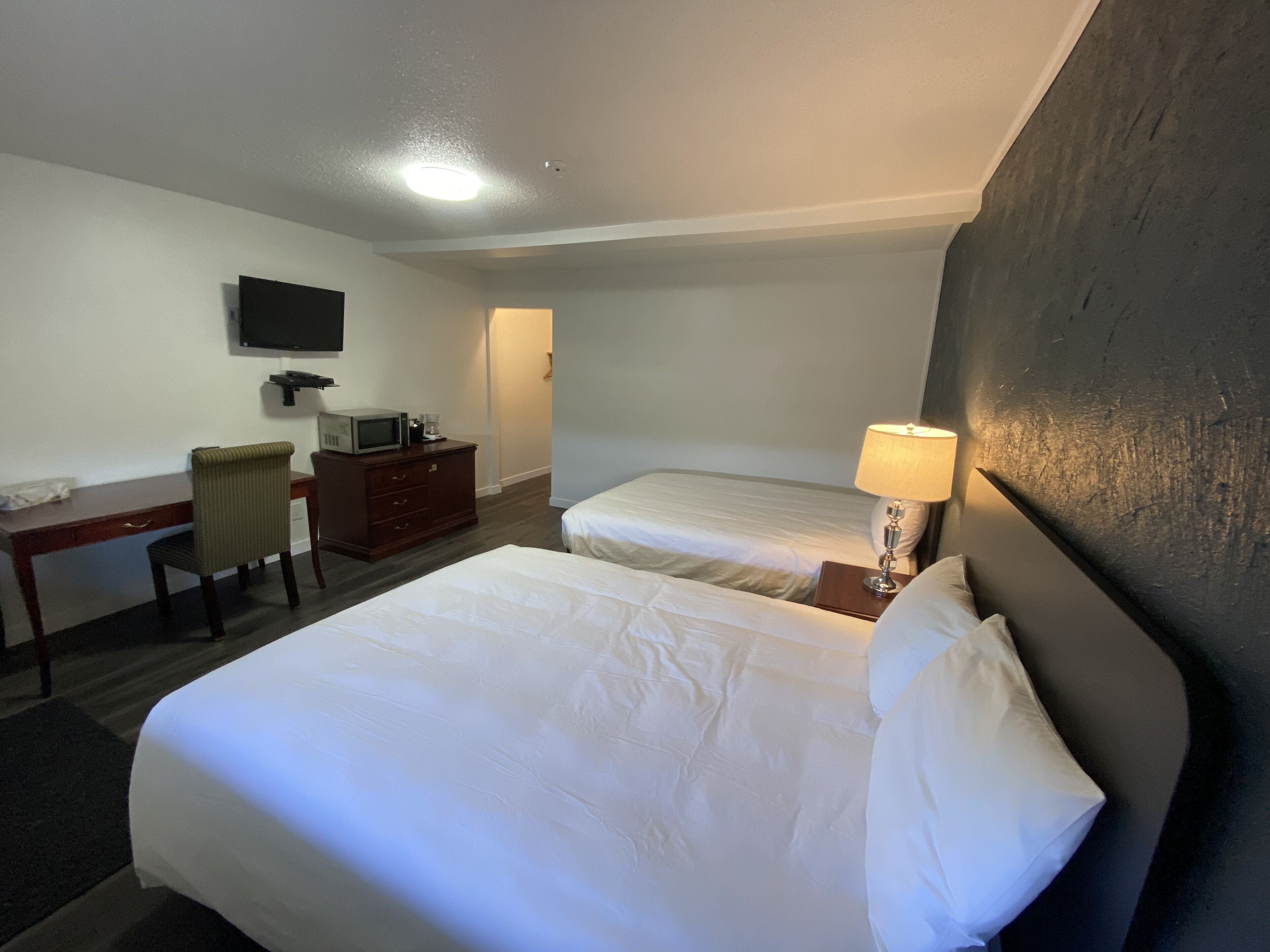 Una habitación de hotel con dos camas, un escritorio con televisor, una silla y una lámpara.