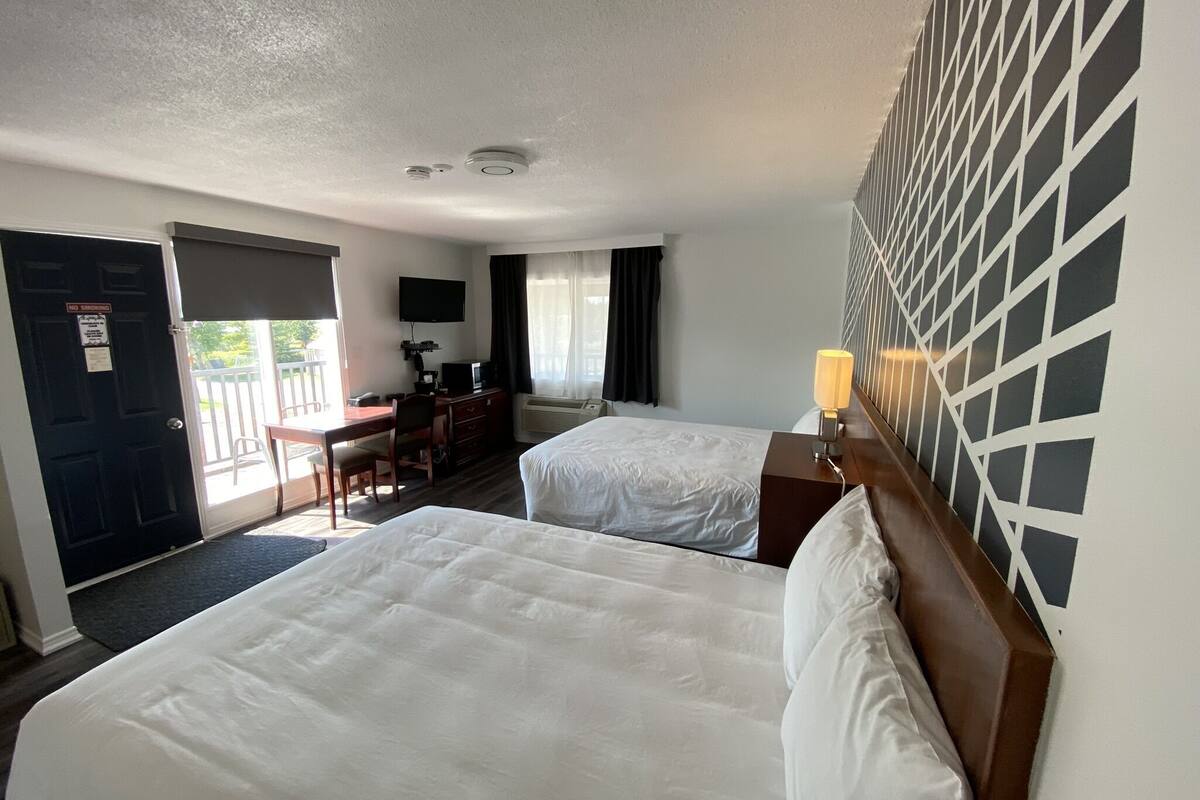 A hotel room with two beds, a desk, a chair, a TV, and a window with curtains.