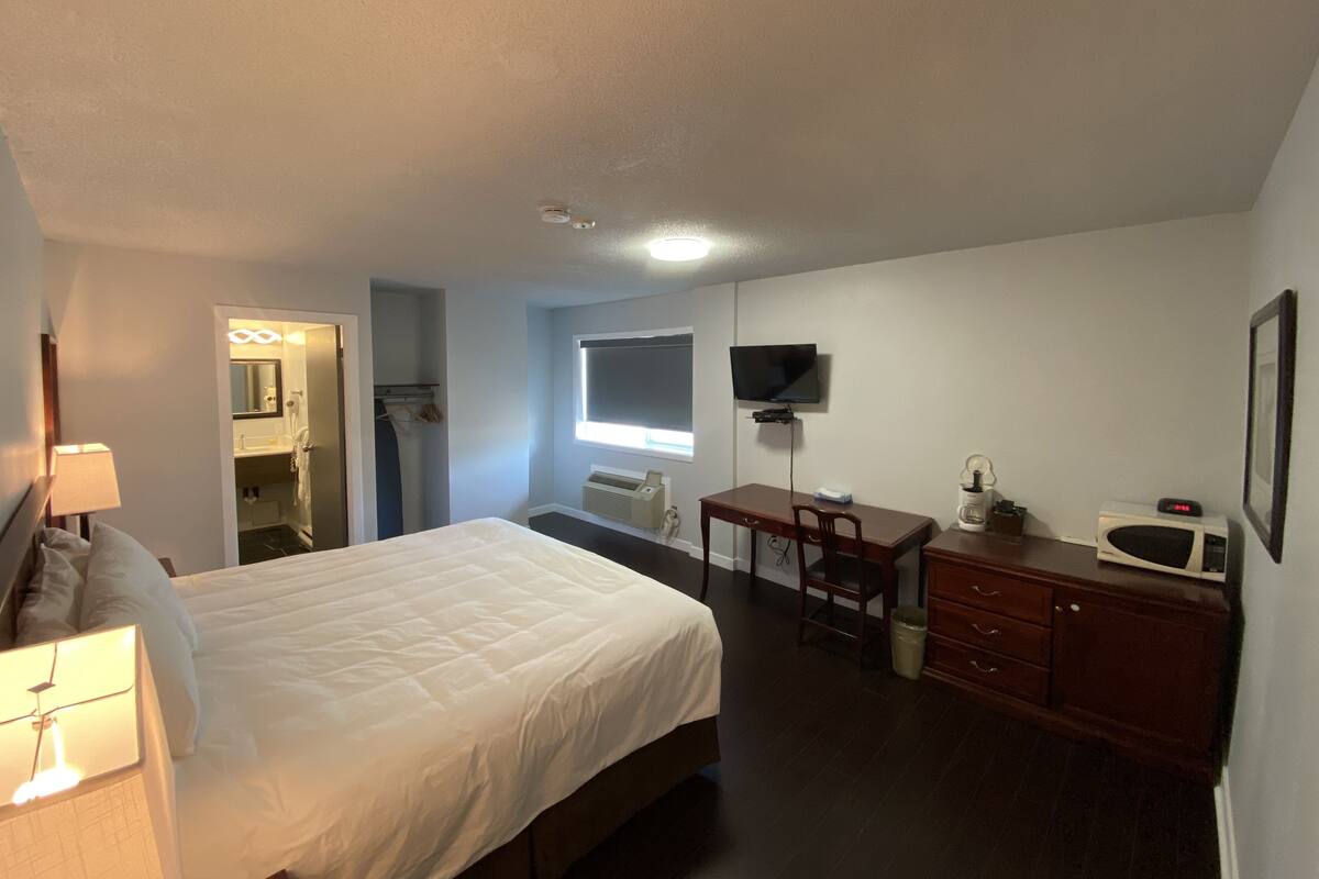 A hotel room with a bed, a desk, a chair, a TV, a microwave, and a wardrobe.