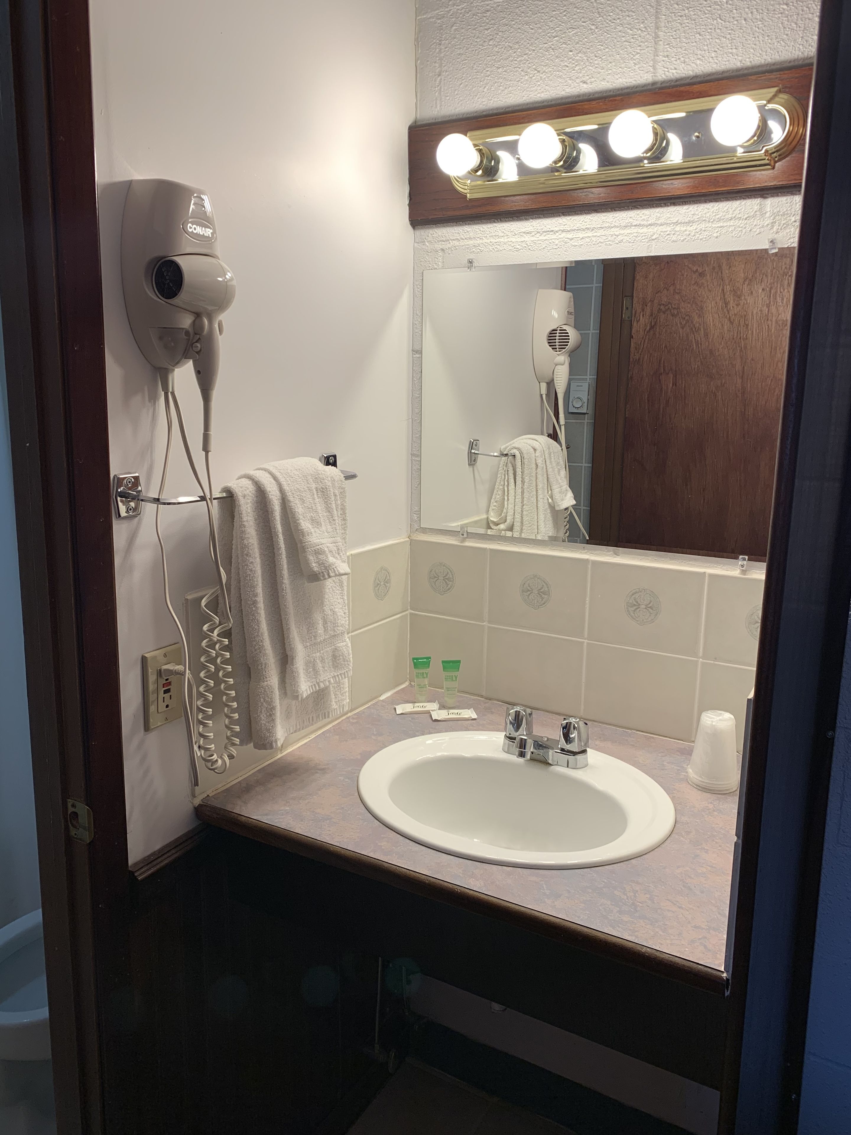 A bathroom with a sink, mirror, hair dryer, and towel rack.