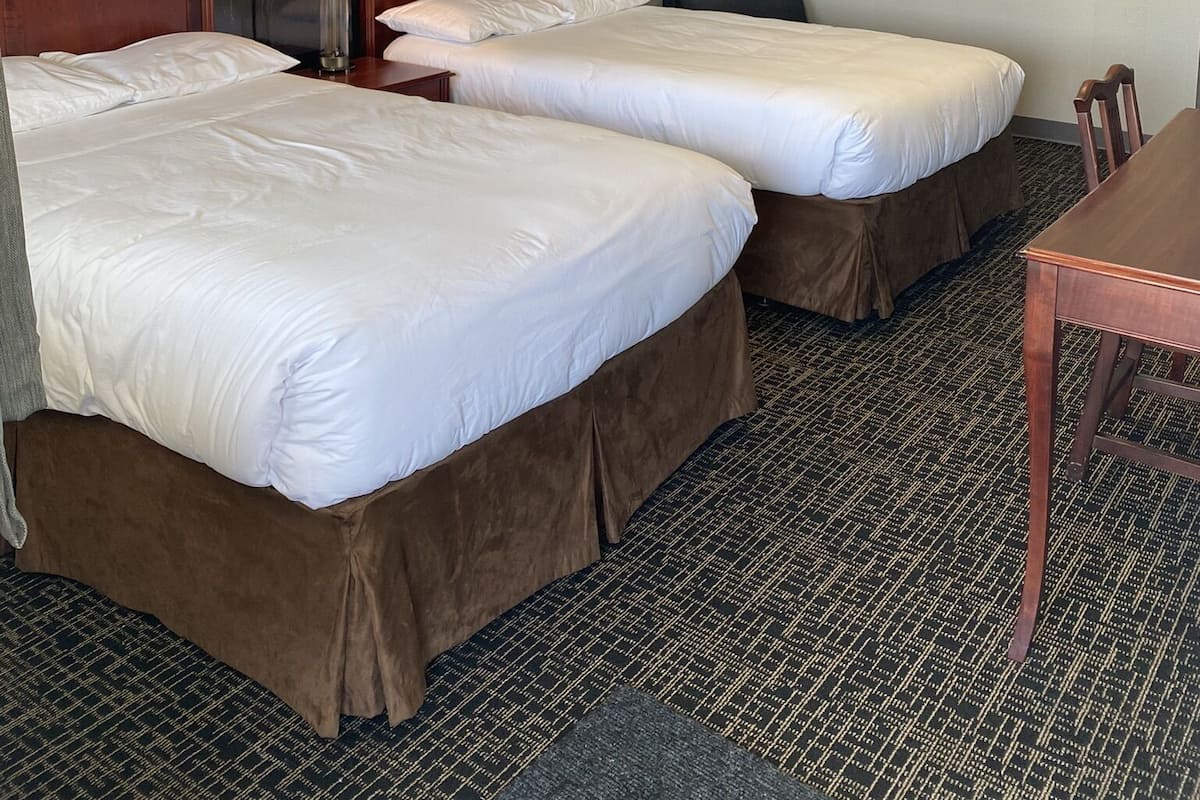 A hotel room with two beds, a desk, a lamp, and a painting on the wall.