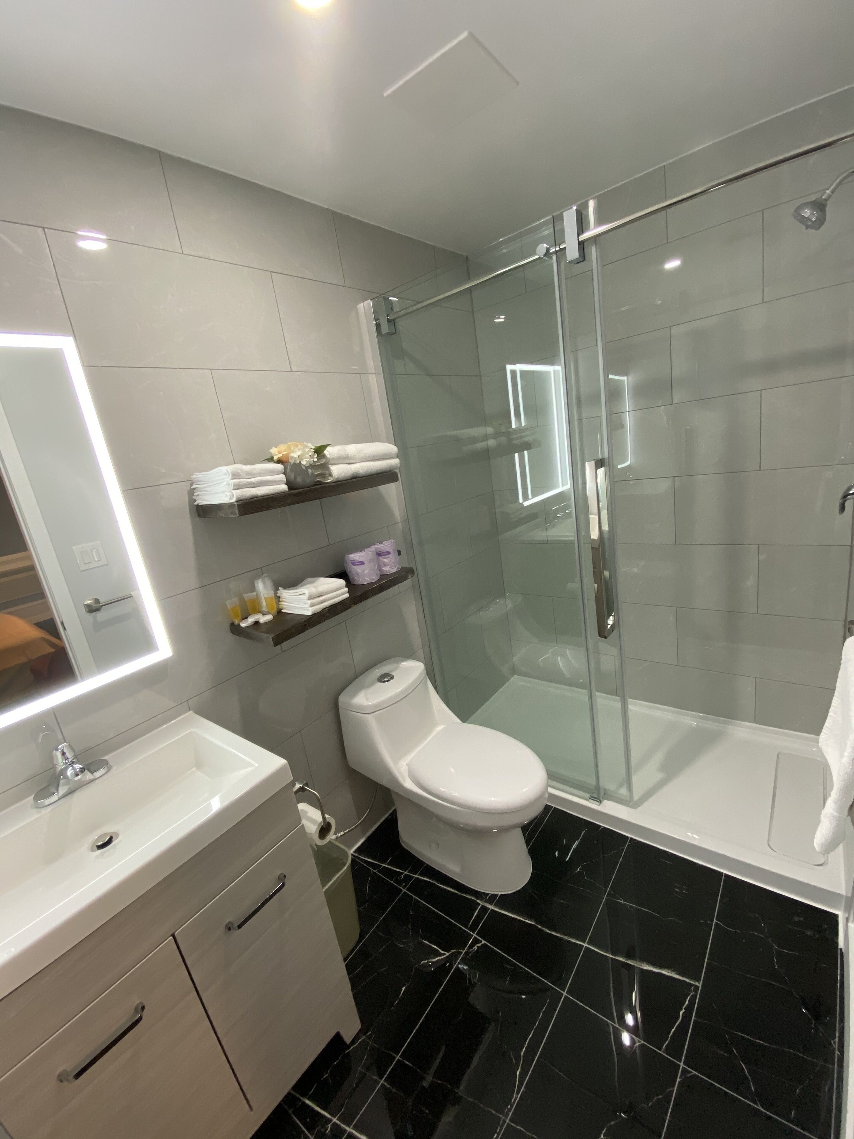 A modern bathroom with a glass-enclosed shower, a white toilet, a vanity with a mirror, and neatly arranged towels on shelves.