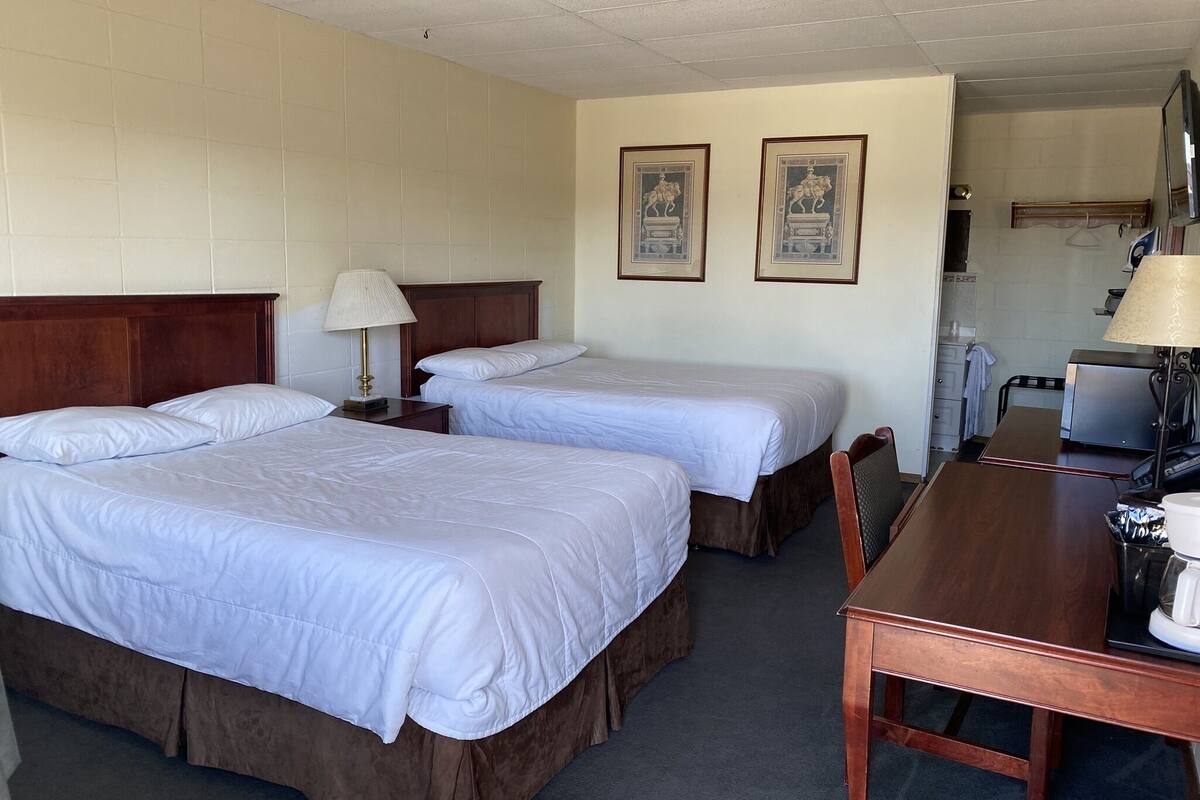 A hotel room with two beds, a wooden desk, a lamp, and a coffee maker.