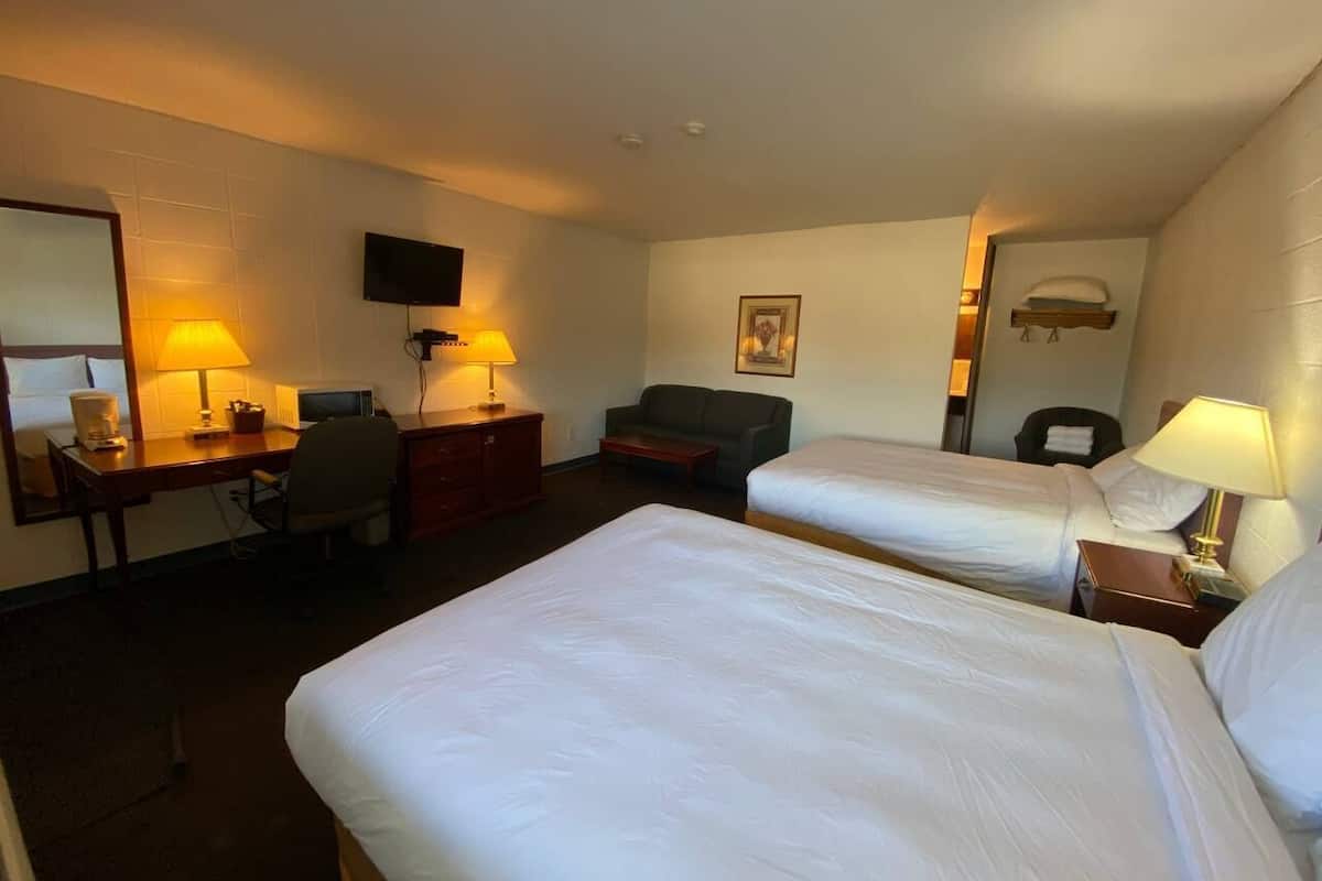 A hotel room with two beds, a desk, a chair, a television, and a sofa.