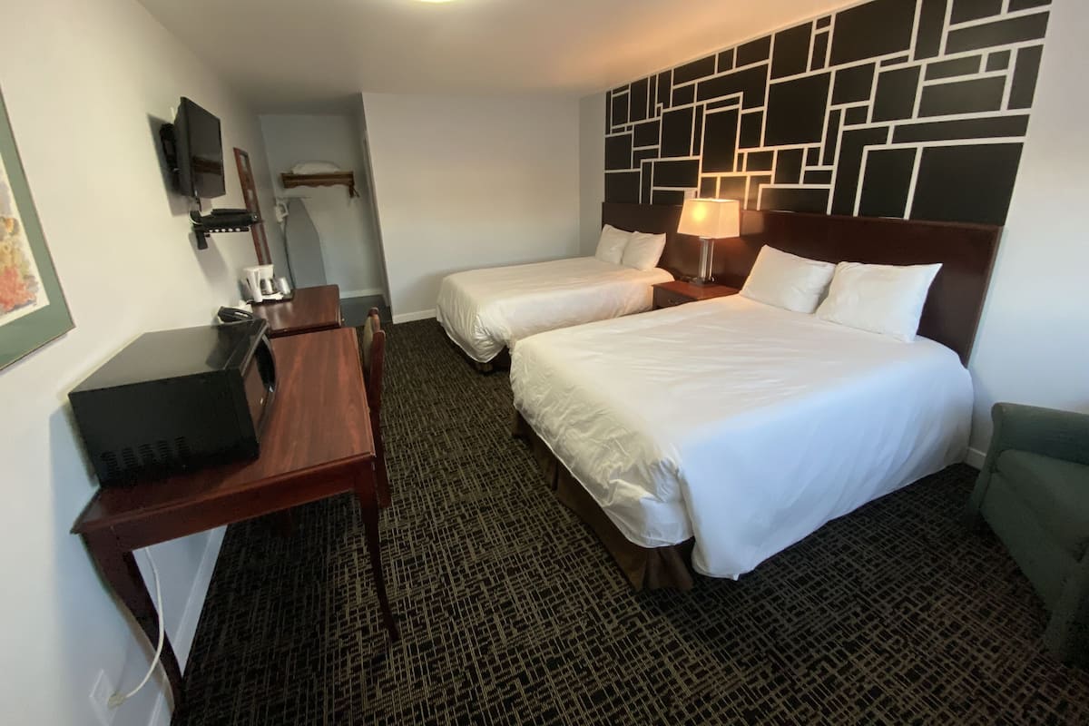 A hotel room with two beds, a desk, a chair, a TV, and a patterned carpet.