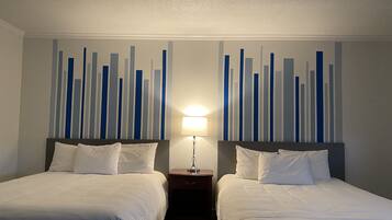 A hotel room with two beds, a nightstand with a lamp, and a wall with vertical blue and white stripes.