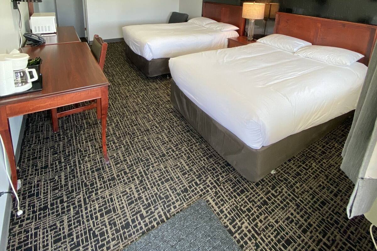 A hotel room with two single beds, a wooden desk with a telephone and a coffee maker, a small table, and a patterned carpet.