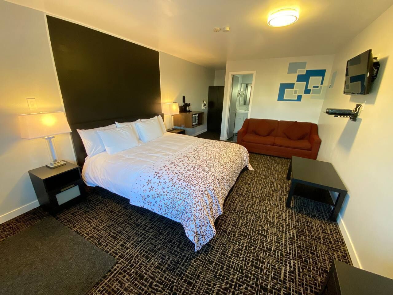 Habitación de hotel con una cama grande, una mesita de noche, un sofá rojo, una pequeña mesa y un televisor montado en la pared.