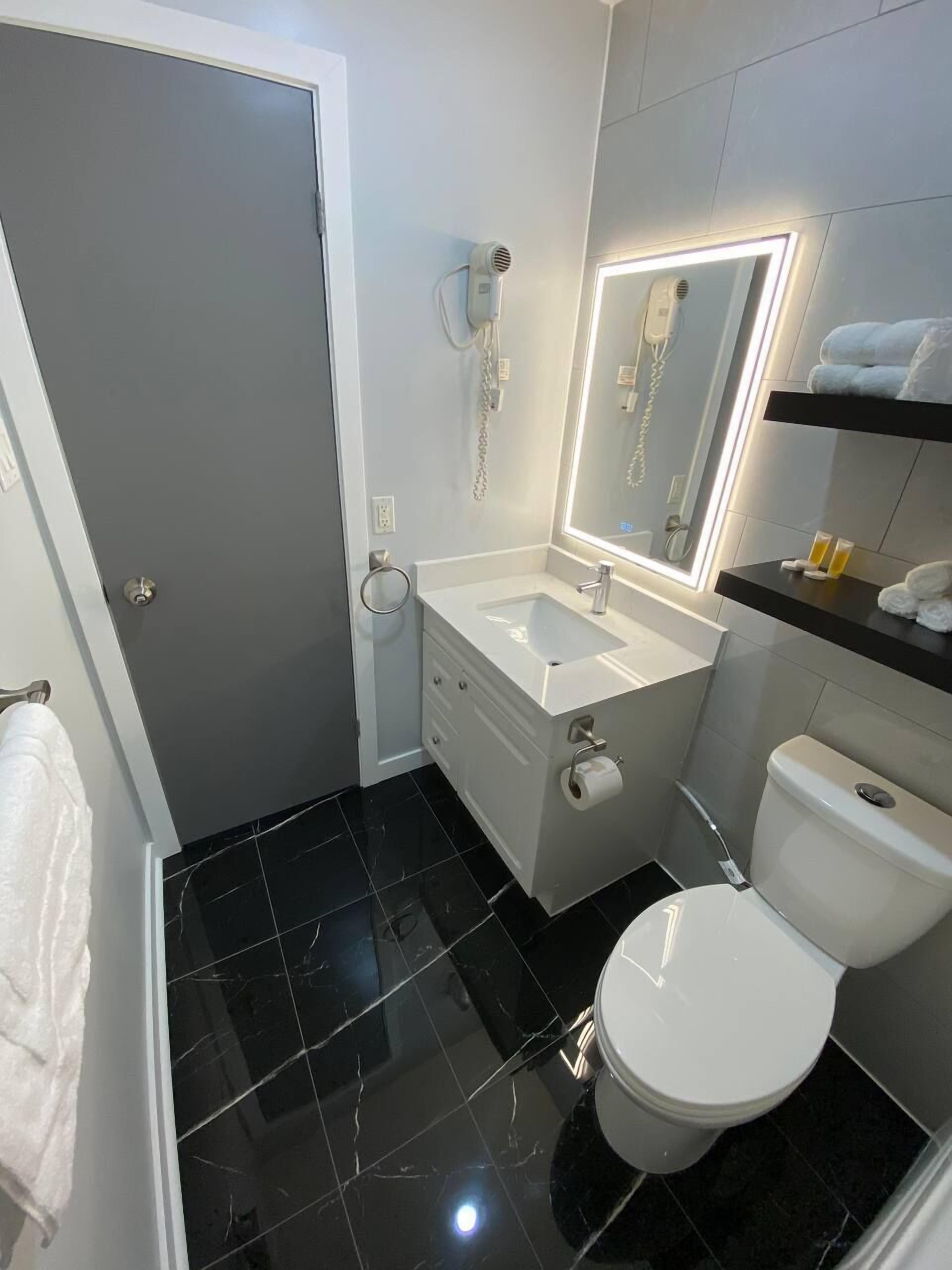 Ein kleines Badezimmer mit einem weißen Waschbecken, einer Toilette und einem Spiegel mit integrierter Beleuchtung.