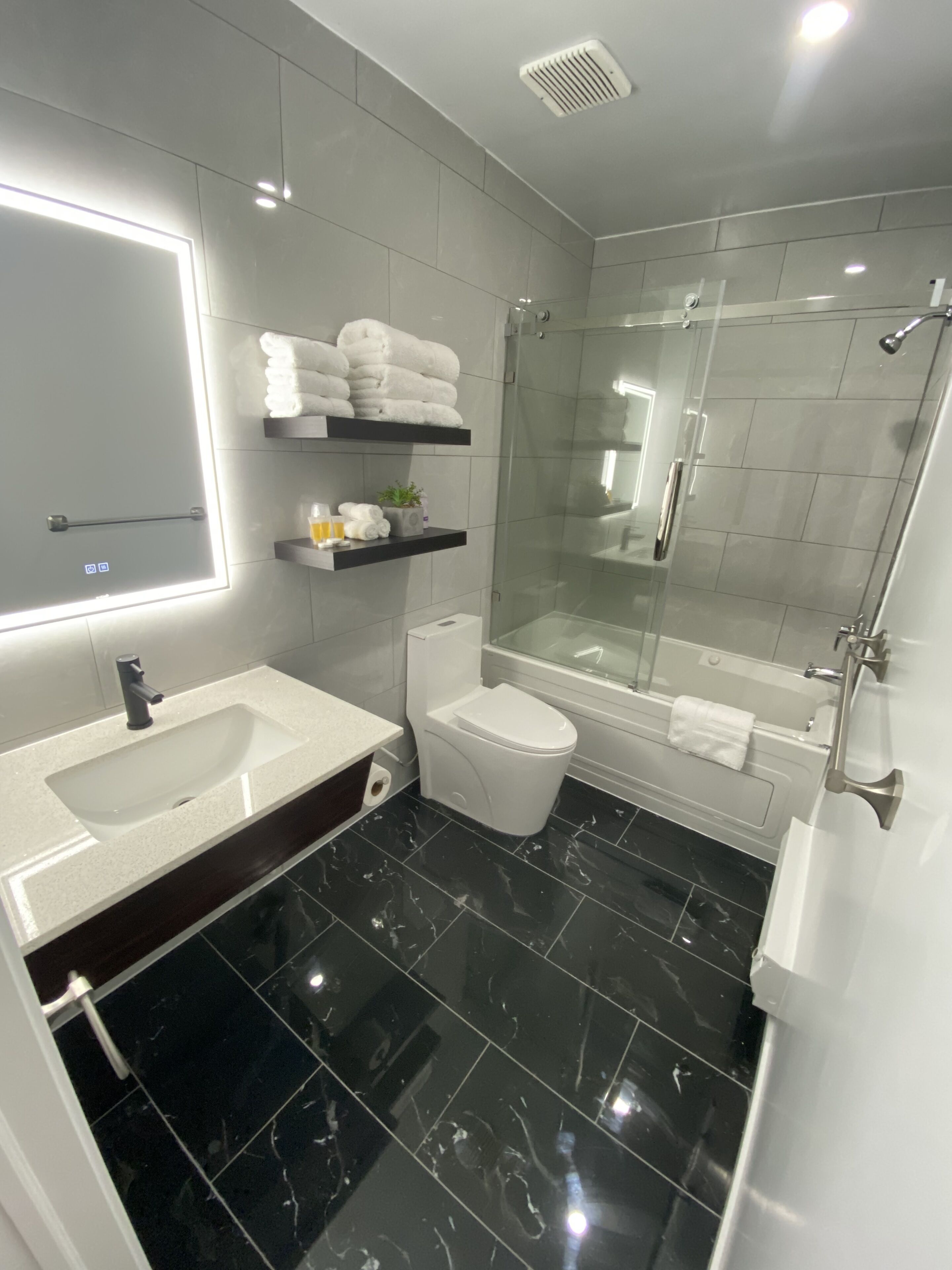 Un baño moderno con un espejo grande, un lavamanos, un inodoro y una ducha con mampara de vidrio.
