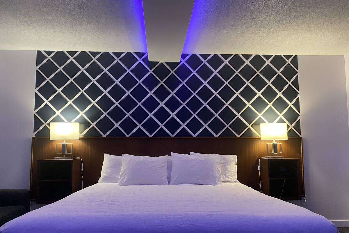 A hotel room with a large bed, two bedside lamps, and a geometric patterned headboard.